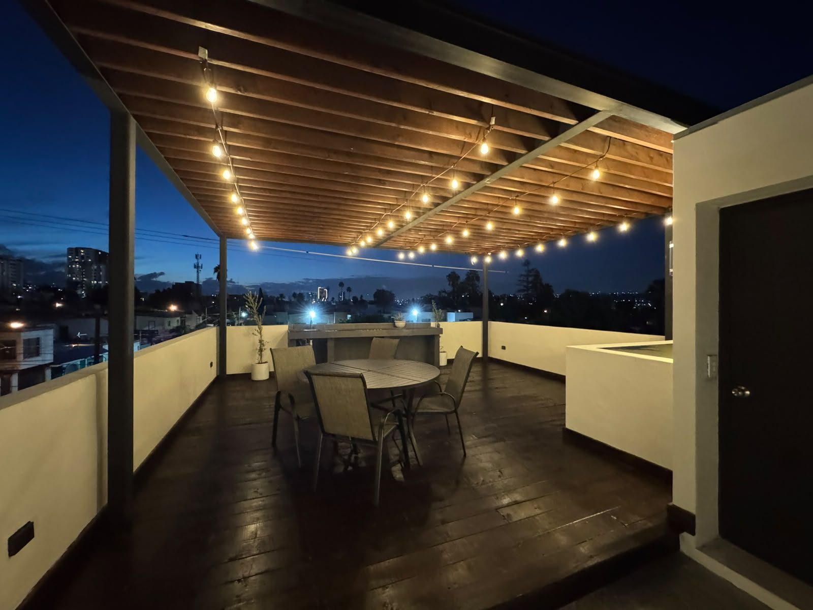 Terraza con pérgola de acero y madera iluminada, con vista nocturna de Tijuana